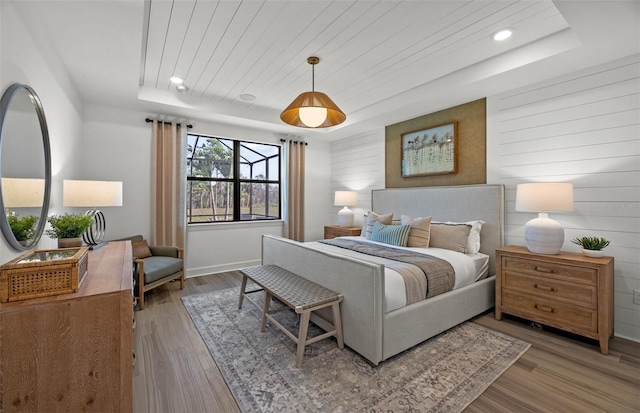 bedroom featuring a raised ceiling, light hardwood / wood-style flooring, wooden walls, and wood ceiling