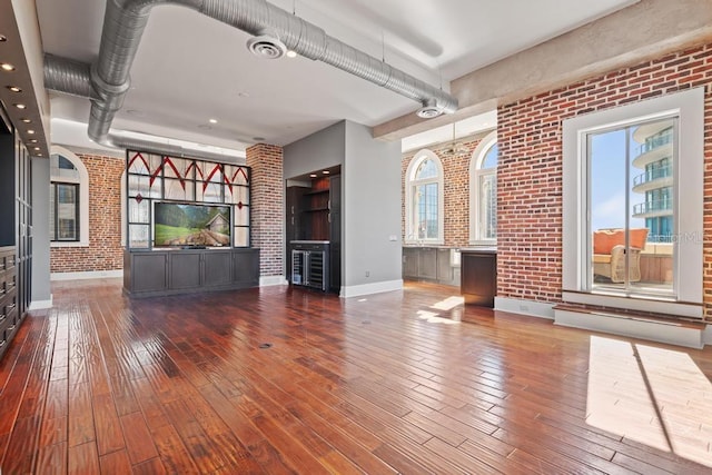 unfurnished living room featuring plenty of natural light, wood-type flooring, and brick wall