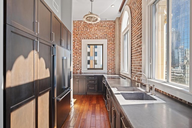 kitchen with dark brown cabinetry, sink, dark wood-type flooring, brick wall, and high quality fridge