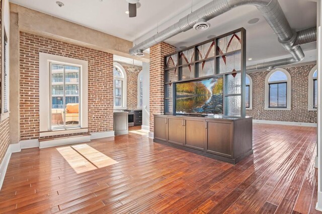 interior space featuring ceiling fan, dark brown cabinetry, wood-type flooring, and brick wall