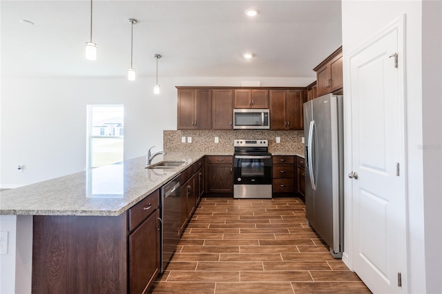 kitchen featuring kitchen peninsula, stainless steel appliances, dark wood-type flooring, sink, and hanging light fixtures