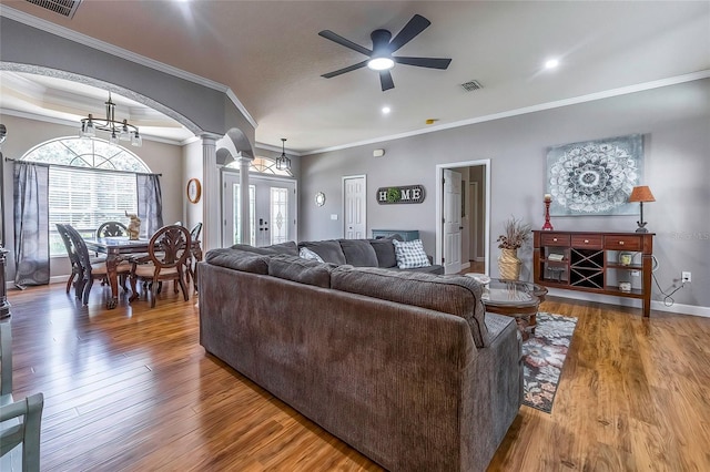 living room featuring decorative columns, crown molding, wood-type flooring, and ceiling fan with notable chandelier