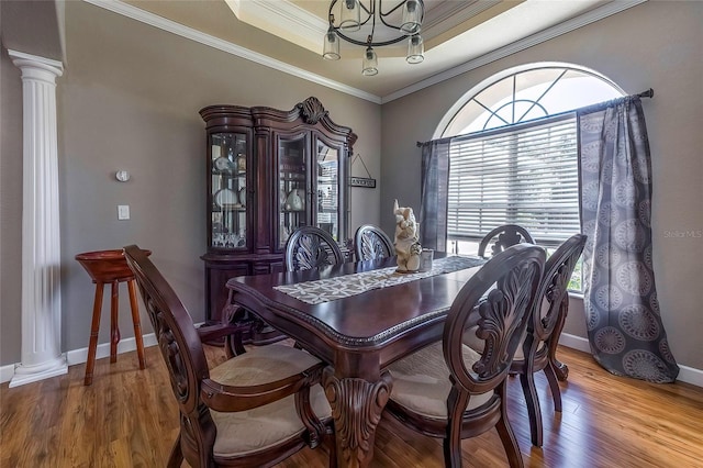 dining space featuring wood-type flooring, decorative columns, a raised ceiling, and ornamental molding