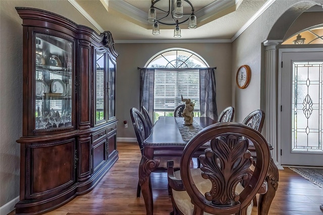 dining area with ornate columns, ornamental molding, a textured ceiling, a tray ceiling, and dark wood-type flooring