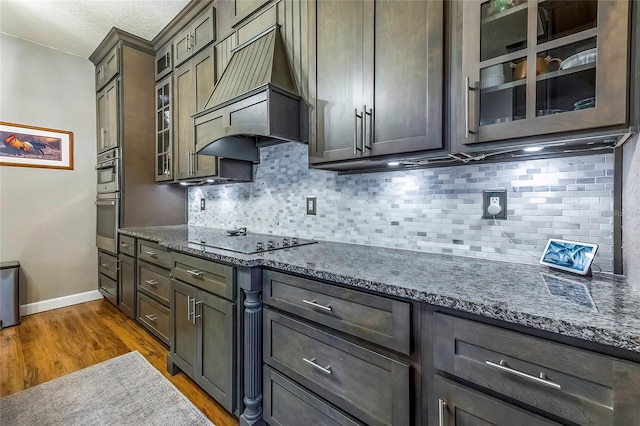 kitchen featuring black electric stovetop, tasteful backsplash, dark stone counters, custom range hood, and dark wood-type flooring