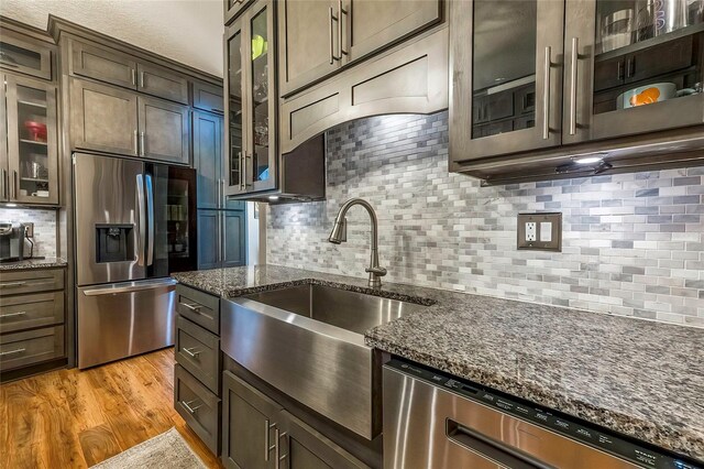 kitchen featuring light wood-type flooring, stainless steel appliances, dark brown cabinetry, and dark stone counters