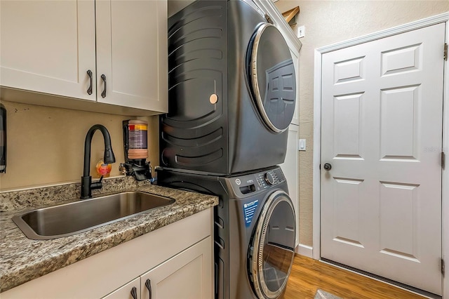 washroom featuring stacked washer / drying machine, cabinets, sink, and light hardwood / wood-style flooring