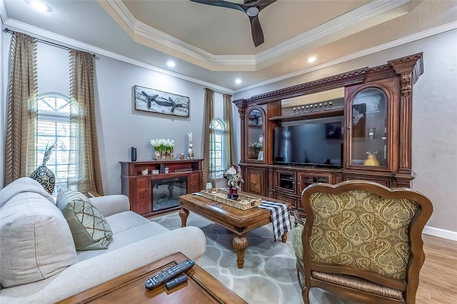 sitting room with a raised ceiling, crown molding, ceiling fan, and light wood-type flooring