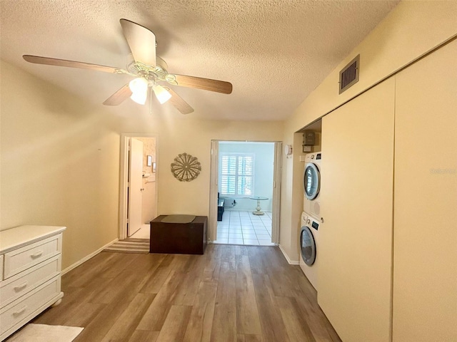 laundry room with wood-type flooring, a textured ceiling, ceiling fan, and stacked washer / drying machine