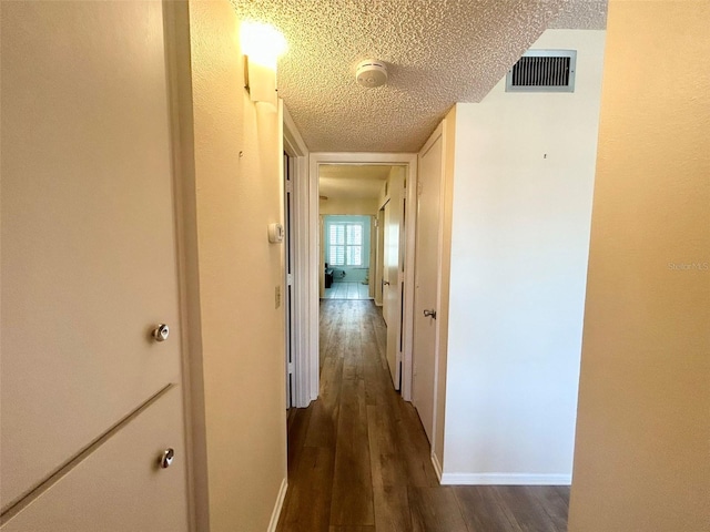 corridor with a textured ceiling and dark wood-type flooring