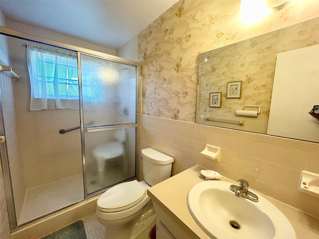 full bath with wallpapered walls, wainscoting, toilet, a shower stall, and tile walls