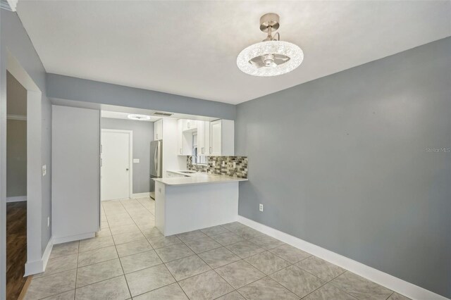 kitchen featuring backsplash, kitchen peninsula, decorative light fixtures, white cabinetry, and stainless steel refrigerator