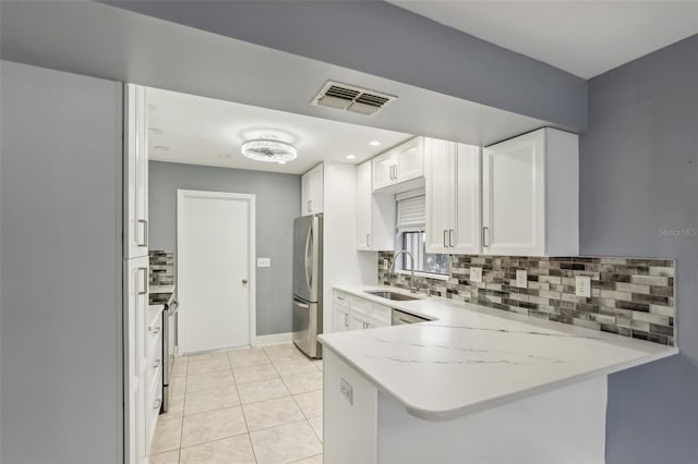 kitchen with sink, white cabinetry, light tile patterned flooring, kitchen peninsula, and stainless steel refrigerator