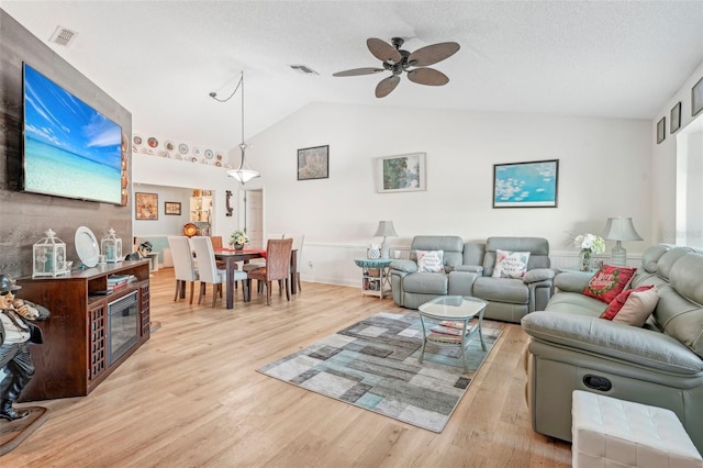 living room with light hardwood / wood-style floors, ceiling fan, vaulted ceiling, and a textured ceiling