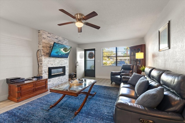 living room with ceiling fan, a fireplace, light hardwood / wood-style floors, and a textured ceiling