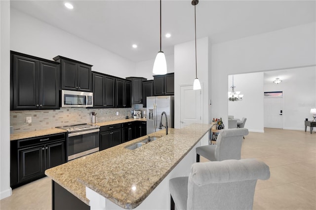 kitchen with a kitchen bar, appliances with stainless steel finishes, hanging light fixtures, and an island with sink