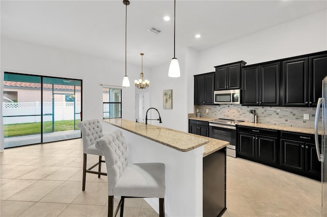 kitchen featuring a kitchen island with sink, a kitchen breakfast bar, hanging light fixtures, tasteful backsplash, and stainless steel appliances