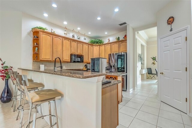 kitchen featuring a breakfast bar, backsplash, crown molding, dark stone countertops, and kitchen peninsula