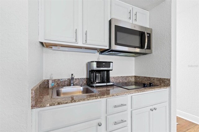 kitchen with white cabinets, black electric cooktop, light hardwood / wood-style flooring, and sink