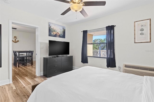 bedroom with a wall mounted AC, light hardwood / wood-style flooring, and ceiling fan