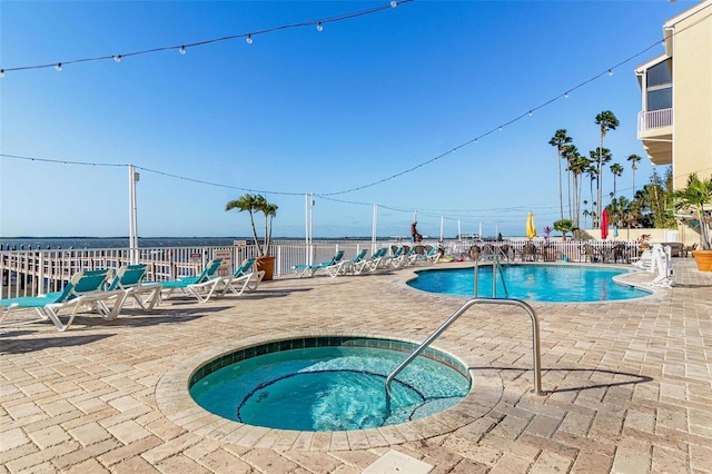 view of swimming pool featuring a water view, a hot tub, and a patio area