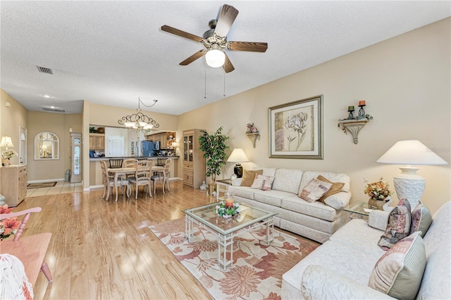 living room with ceiling fan with notable chandelier, light hardwood / wood-style floors, and a textured ceiling