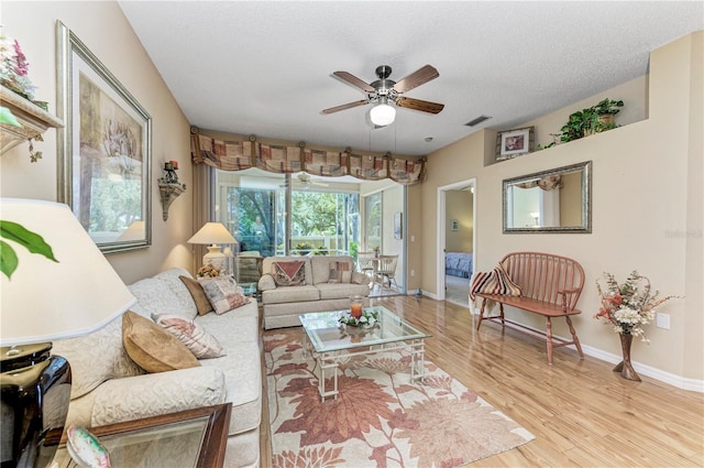 living room with ceiling fan, light wood-type flooring, and a textured ceiling