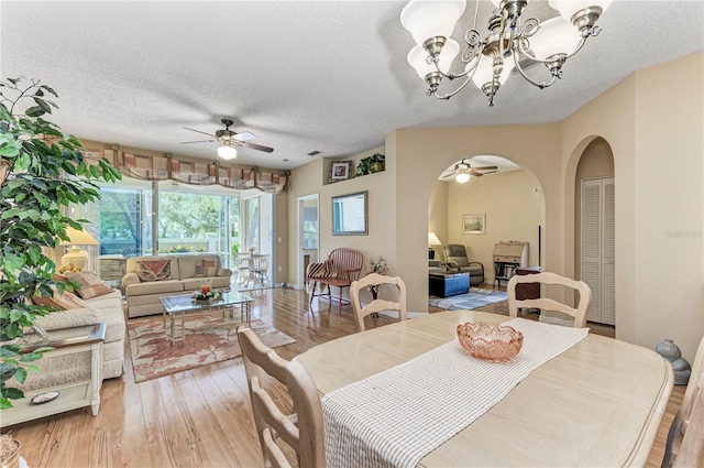 dining room featuring ceiling fan with notable chandelier, light wood-type flooring, and a textured ceiling