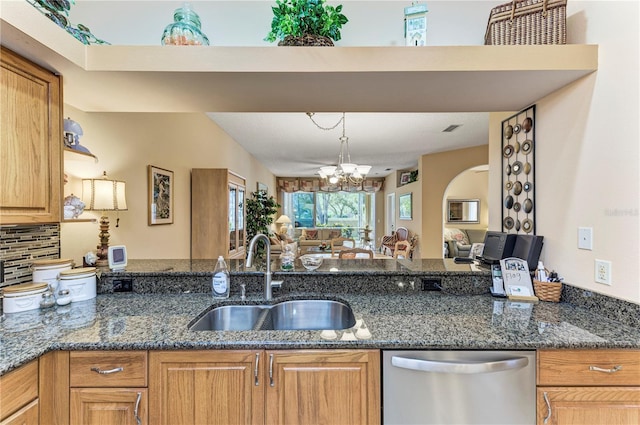 kitchen with tasteful backsplash, stainless steel dishwasher, dark stone counters, sink, and an inviting chandelier