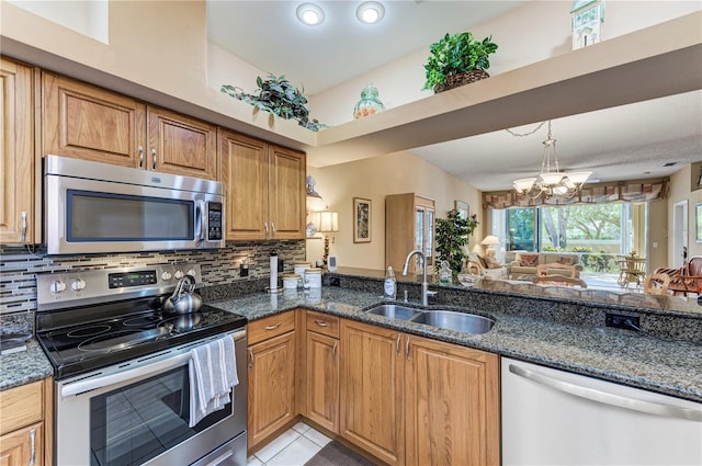 kitchen featuring dark stone countertops, stainless steel appliances, a notable chandelier, and sink