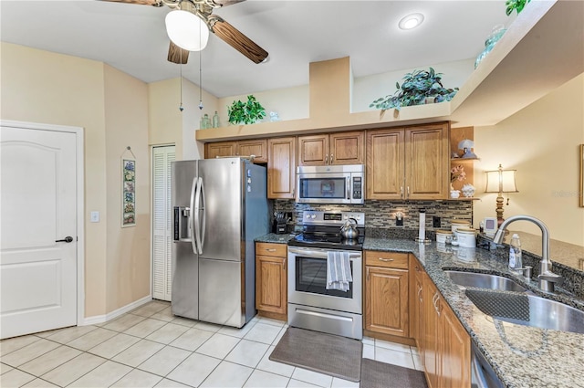 kitchen with sink, ceiling fan, dark stone countertops, light tile patterned floors, and appliances with stainless steel finishes