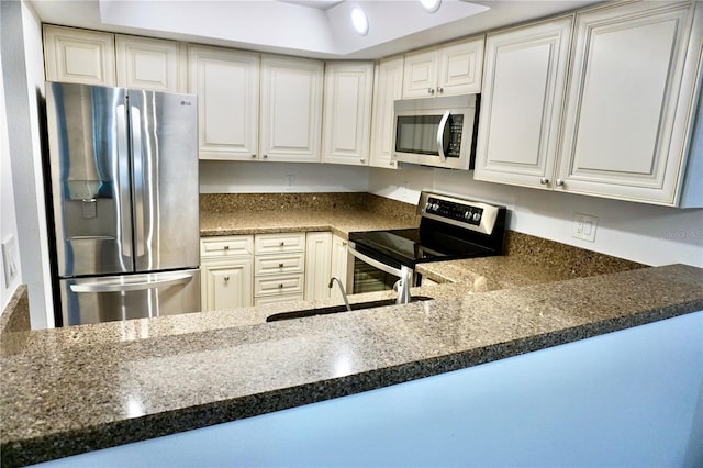 kitchen with kitchen peninsula, appliances with stainless steel finishes, white cabinetry, and sink