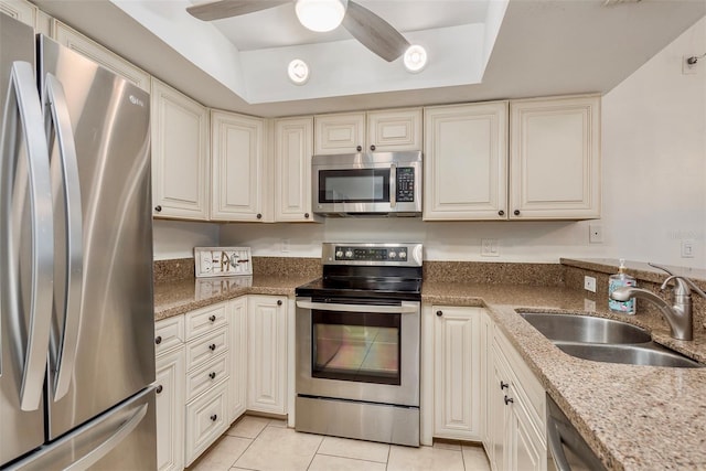 kitchen with light stone counters, stainless steel appliances, a raised ceiling, sink, and light tile patterned flooring