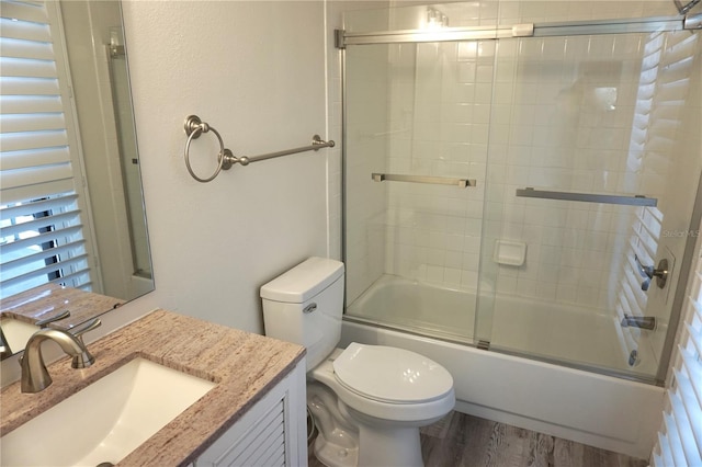 full bathroom with hardwood / wood-style flooring, vanity, toilet, and bath / shower combo with glass door