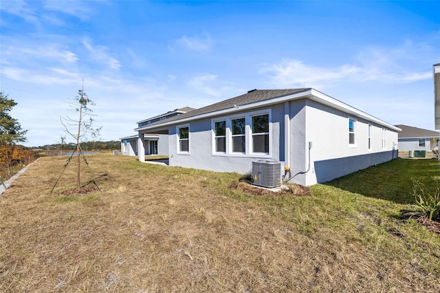 rear view of house with central AC unit and a lawn