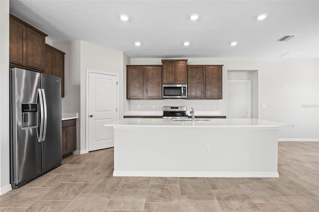 kitchen with dark brown cabinetry, stainless steel appliances, a kitchen island with sink, and sink