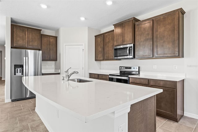 kitchen with dark brown cabinets, a textured ceiling, stainless steel appliances, a kitchen island with sink, and sink