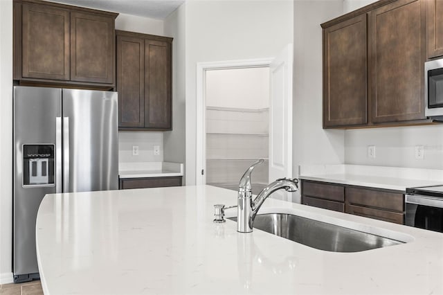 kitchen featuring appliances with stainless steel finishes, light stone counters, dark brown cabinets, and sink