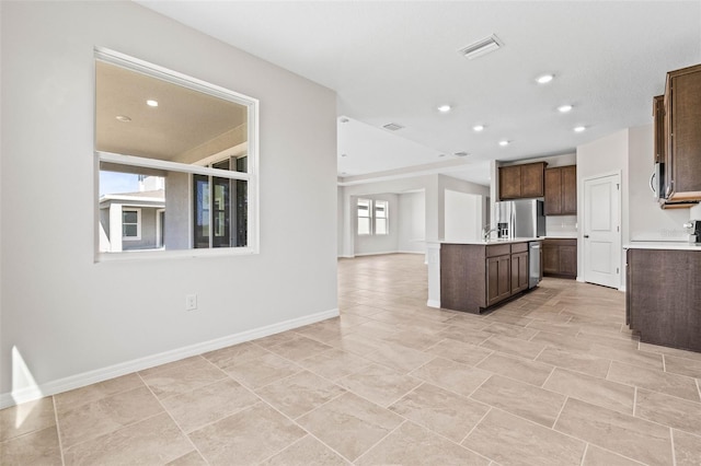 kitchen with dark brown cabinets, stainless steel fridge with ice dispenser, and a kitchen island with sink