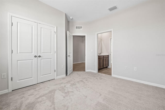 unfurnished bedroom featuring light carpet, ensuite bathroom, and a closet