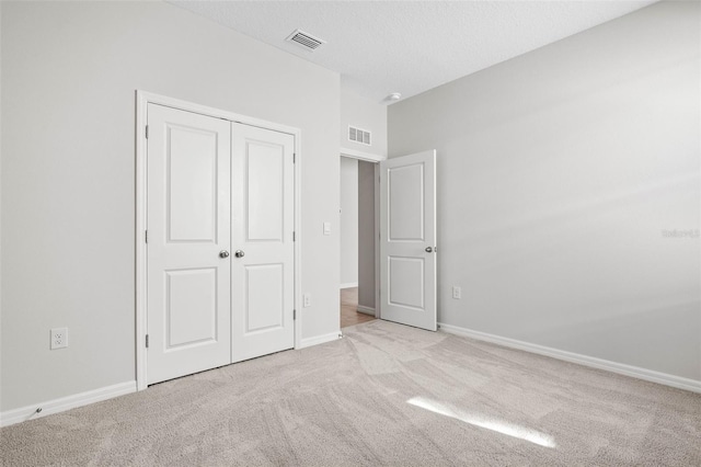 unfurnished bedroom featuring light carpet, a closet, and a textured ceiling