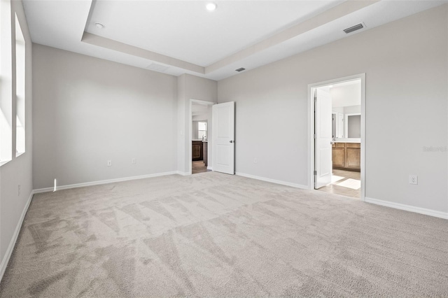 unfurnished bedroom with a raised ceiling, light colored carpet, and ensuite bath