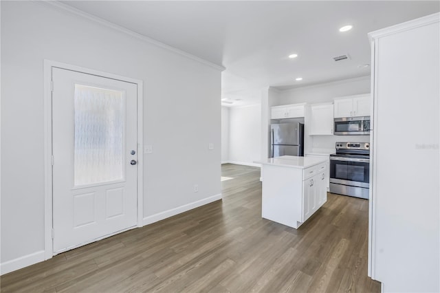 kitchen with white cabinetry, ornamental molding, appliances with stainless steel finishes, a kitchen island, and hardwood / wood-style flooring