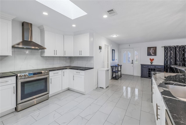 kitchen featuring a skylight, wall chimney exhaust hood, tasteful backsplash, stainless steel range with electric stovetop, and white cabinets