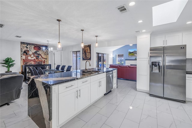 kitchen featuring pendant lighting, dark stone counters, an island with sink, appliances with stainless steel finishes, and white cabinetry