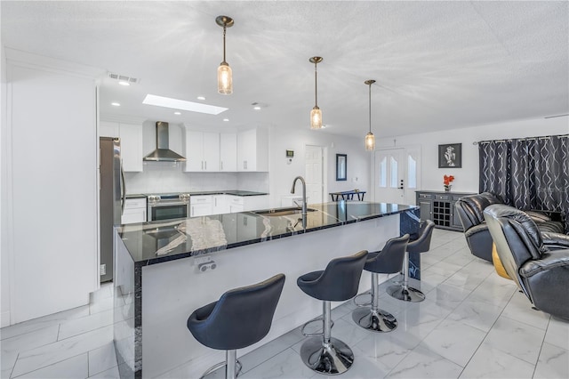 kitchen featuring pendant lighting, a skylight, wall chimney exhaust hood, and sink