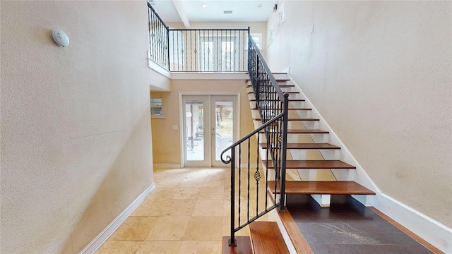 stairway with french doors, a towering ceiling, and baseboards