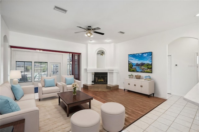 living room with a tile fireplace, ceiling fan, and light wood-type flooring