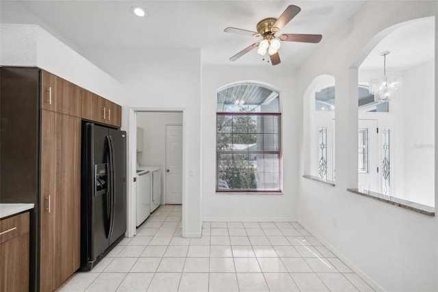 kitchen with washing machine and dryer, black fridge, decorative light fixtures, light tile patterned floors, and ceiling fan with notable chandelier