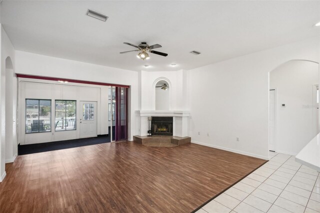 unfurnished living room featuring a tile fireplace, ceiling fan, and light hardwood / wood-style floors